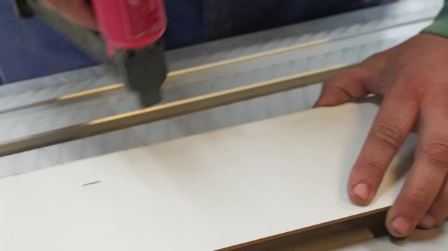 Carpenter nailing a wooden panel with a pneumatic nail gun