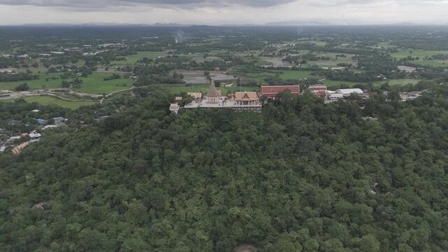 Aerial drone view of Wat Sangkat Rattana Khiri on Sakae Krang Hill in Uthai Thani, Thailand. Majestic golden Buddhist temple complex nestled in lush green forest overlooking rural rice fields and town