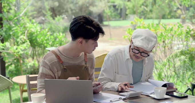 Asian father and son discuss cafe accounting paperwork, calculator, tablet, sales note, daily summary, family restaurant mentoring, practical training for next generation owner mindset and duty.