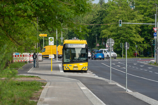 Germany, Berlin May 22, 2026 A yellow city bus waits at a tree lined stop beside a busy road. Deciduous trees and spring foliage frame the Berlin transport scene.
