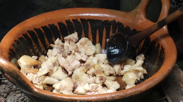 Chef stirring cooked pork meat pieces inside a traditional hot clay cazuela pot