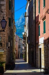 Fototapeta premium Cozy old alley in Makarska surrounded by historic stone buildings and dramatic Dalmatian mountains. A romantic European travel destination perfect for authentic local experience, cultural tourism.