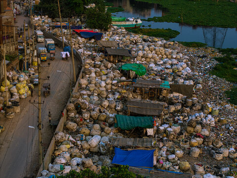 Aerial view of the Buriganga River bank filled with thousands of recycling bags and makeshift shelters under colorful tarps in Keraniganj, Dhaka Division, Bangladesh.