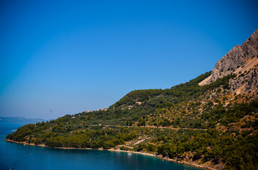 Obraz premium Scenic Adriatic shoreline framed by Mediterranean pine forest and rugged coastal rocks on the Makarska Riviera. A peaceful Croatian travel destination perfect for tourism promotions, slow travel story
