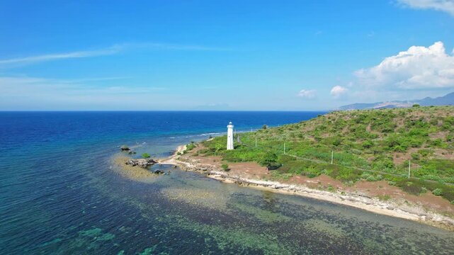 Aerial drone footage of Rambu Suar Batu Besar lighthouse, at the edge of a coastal dry road in Soromandi area, Bima regency, Sumbawa island, Indonesia, with blue sea waters and reefs, white sand beach
