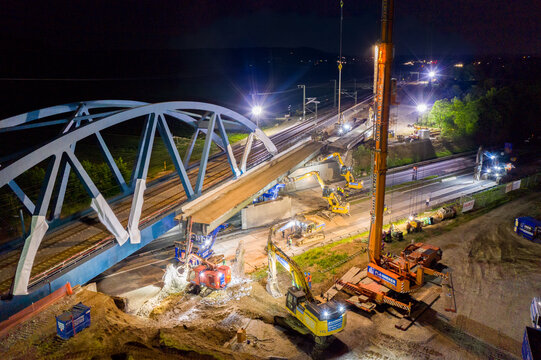 Forchheim, Germany - 18 May 2024: Aerial view of construction work on the A73 bridge at night with heavy machinery, cranes, and bright floodlights illuminating the site.