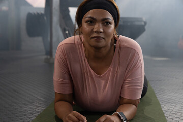 African American female holding forearm plank on green mat in gym wearing pink top and headband © wavebreak3