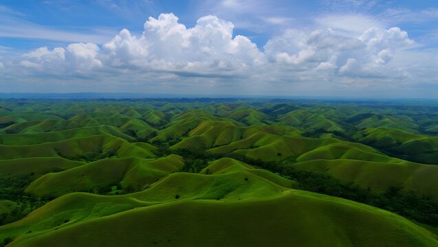 Vast expanse of lush green rolling hills stretches out under a partly cloudy blue sky