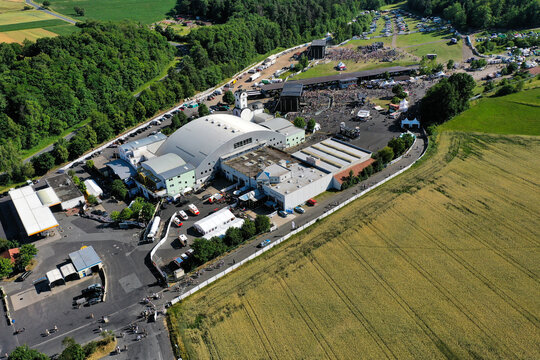 Geiselwind, Germany - 21 June 2025: Aerial view of Eventzentrum Strohofer Geiselwind musichall with outdoor stages, crowds of people, and surrounding green fields under a clear sky.