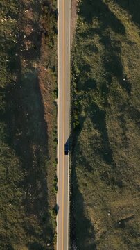 Vertical Screen: Beartooth Highway in Montana USA as a lone car travels along winding mountain road. Drone captures the golden hour light casting long shadows across rocky terrain and green meadows.