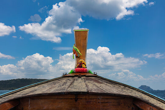 Prow of a longtail boat in the Andaman Sea near Krabi, Thailand. Cloudy blue sky ahead over the horizon.
