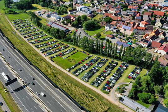 Geiselwind, Germany - 21 June 2025: Aerial view of Eventzentrum Strohofer Geiselwind musichall with a large parking lot full of cars next to the highway and residential houses.