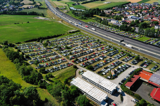 Geiselwind, Germany - 21 June 2025: Aerial view of Eventzentrum Strohofer Geiselwind musichall parking lot filled with cars next to the A3 highway, surrounded by green fields.