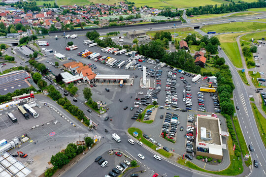 Geiselwind, Germany - 20 June 2025: Aerial view of a busy highway service area and truck stop with numerous parked trucks, cars, a gas station, and commercial buildings.