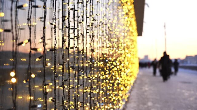 Golden string lights decorating building exterior with blurred people walking during winter