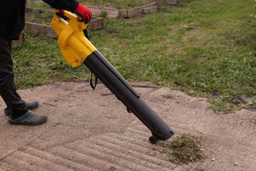 Worker uses electric blower to clear debris from garden path