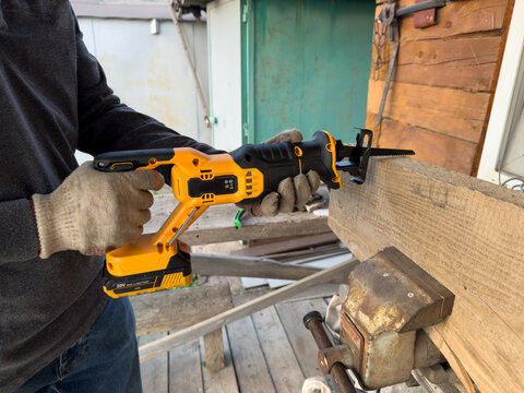 Handheld sabre saw with blade cutting scrap wood outdoors