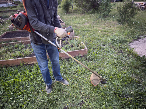 Worker uses electric brushcutter to trim overgrown garden grass