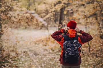 Naklejka premium Rear view of woman hiker adjusting hat while standing in autumn forest. nature-based therapy, mental resilience outdoors, forest bathing benefits.