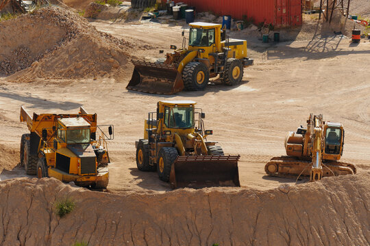 Multiple construction and mining vehicles working inside an active open pit quarry. Heavy machinery performs excavation and material transport across industrial extraction site.