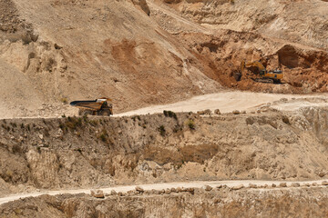 Heavy excavator loading mining dump truck inside active limestone quarry with terraced excavation levels and haul roads. Industrial mining operation showing earthmoving and raw material extraction  © Ekaterina