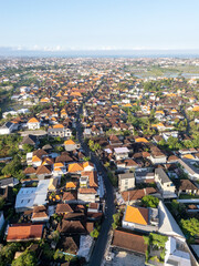 Obraz premium Aerial panoramic view of a dense Balinese town with traditional terracotta tile roofs, a main street, and distant ocean in sunlight at Canggu, Bali, Indonesia