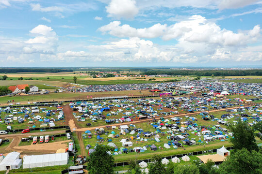 Herzogenaurach, Germany - 27 July 2025: Aerial view of the Open Beatz Festival campsite featuring rows of colorful tents, a large parking area, and expansive green fields under a bright cloudy sky.
