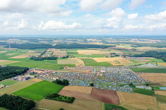 Herzogenaurach, Germany - 27 July 2025: Aerial view of the Open Beatz Festival site with numerous tents and stages set amidst agricultural fields and forests under a cloudy sky.