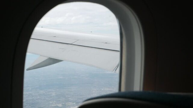 Aerial view through plane window with view of airplane wing over puffy white cloud with clear blue sky while flying, View from the window of the plane traveling by air, vacation background concept