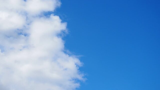 Bright clouds move across blue sky on sunny day. Time is during midday when light is strong and clear. Atmosphere shows natural beauty in simple way. One half of sky is blue, other half is in clouds.