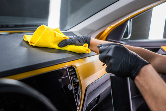 Cleaner hands cleaning car dashboard with yellow cloth and spray, interior car wash and vehicle cleaning concept
