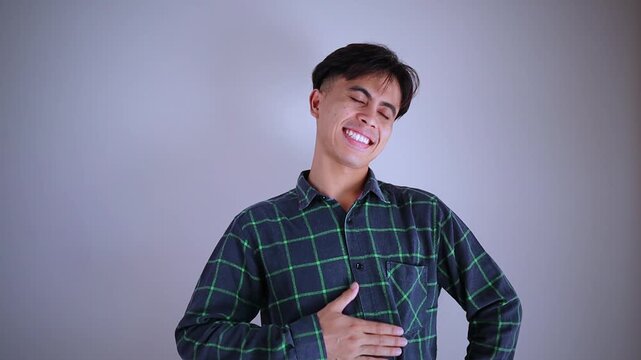 Happy young Asian man smiling and holding his stomach with a look of relief, expressing comfort and wellness in a bright studio background.