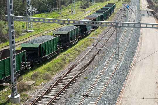 Green freight wagons loaded with ballast gravel near newly reconstructed railway tracks and electric rail infrastructure.