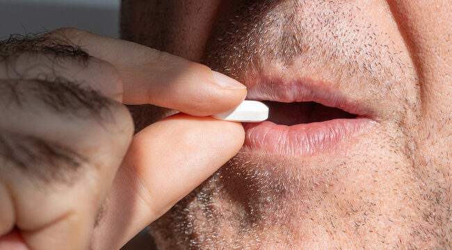 An unshaven puts a pill in his mouth in
