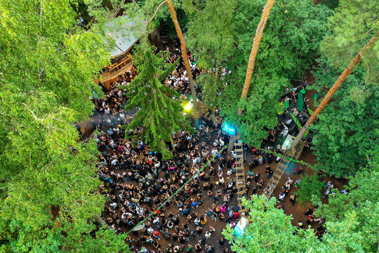 Herzogenaurach, Germany - 26 July 2025: Aerial view of Open Beatz Festival with a large crowd of people dancing in a forest clearing surrounded by dense green trees.