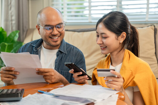 Young couple in the story begin their life together planning their future and managing finances and expenses. Happy Asian husband and wife calculating income and bills to plan for investment.