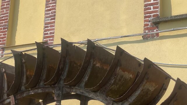 Water Wheel Detail: A close-up view reveals the weathered wooden paddles of a water wheel against a textured yellow wall, hinting at rustic charm and historical engineering.