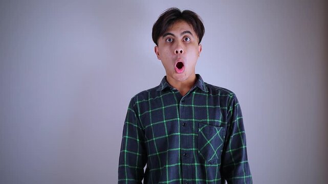 Surprised young Asian man looking at camera with funny shocked face expression, amazed guy reacting to unexpected good news or shock promo concept