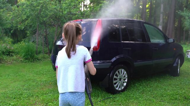 Little girl washes car with pressure washer outdoors in nature. High pressure car wash