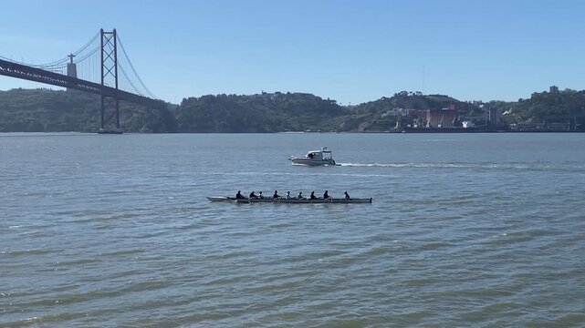 Rowing team training on Tagus river with a large suspension bridge in Lisbon Portugal