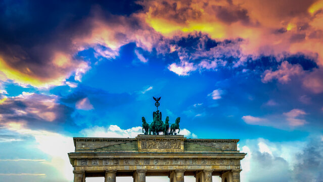 Brandenburg Gate in Berlin illuminated by colorful sunset sky with dramatic clouds