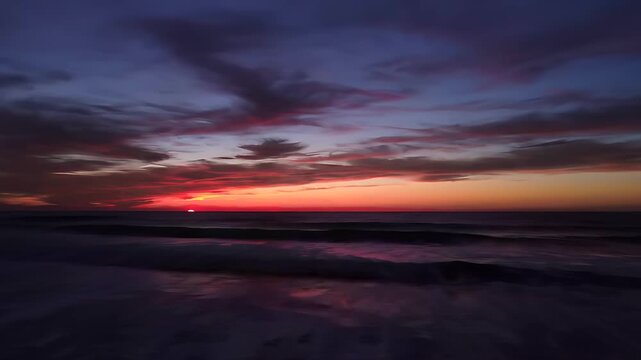 Vibrant sunset over ocean waves transitioning into deep purple twilight. Dramatic evening coastal landscape with colorful clouds. Nature background for travel and wellness marketing.