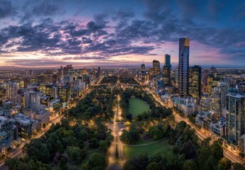 Obraz premium Panoramic Aerial View of a Bustling Cityscape at Dusk with a Lush Green Park Illuminated by City Lights Under a Dramatic Purple and Orange Cloudy Sky