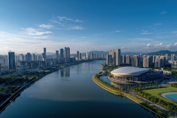 Naklejka premium Panoramic Aerial View of a Modern Cityscape with a Wide River Reflecting the Blue Sky and White Clouds During Golden Hour with a Large Stadium on the Right Bank Overlooking the Water and Distant