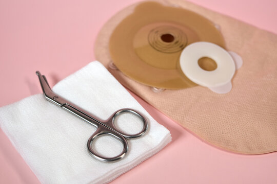 Ostomy care supplies with pouch, scissors and sterile gauze on pink background, illustrating postoperative medical hygiene and care.