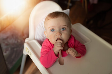 Fototapeta premium Baby with blue eyes sitting in high chair holding spoon