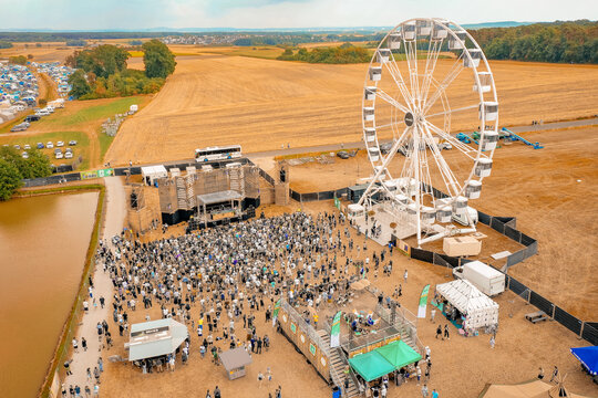 Herzogenaurach, Germany - 22 July 2022: Aerial view of the Open Beatz Festival featuring a large white Ferris wheel, a stage, and a crowd of people surrounded by golden fields.