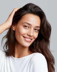 Naklejka premium Beautiful young brunette woman touching hair and smiling softly, neutral gray studio backdrop, beauty portrait lighting