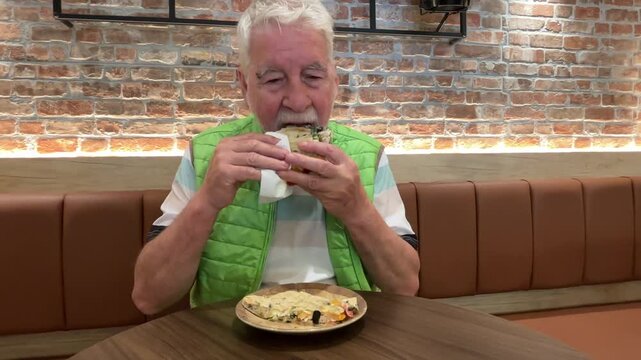 Senior Man Enjoys Delicious Sandwich Alone at a Cozy Cafe Table During Lunchtime