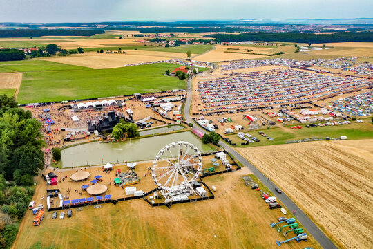 Herzogenaurach, Germany - 22 July 2022: Aerial view of the Open Beatz Festival featuring a Ferris wheel, multiple stages, and large crowds of people surrounded by agricultural fields.